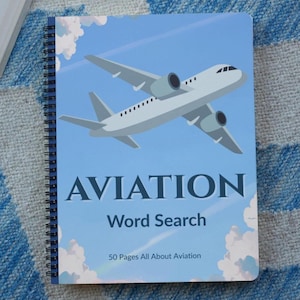 Könnte beinhalten: Spiralgebundenes Notizbuch mit Aviation-Thema. Der blaue Einband zeigt ein weißes Flugzeug vor blauem Himmel mit Wolken. Auf dem Cover steht "AVIATION Word Search" und "50 Pages All About Aviation".