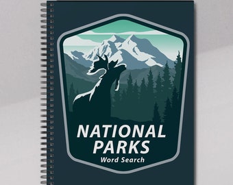 Może przedstawiać: Ciemnoniebieski notatnik spiralny z grafiką łosia na tle gór i drzew iglastych. Napis NATIONAL PARKS Word Search widnieje białymi literami wewnątrz tarczy w kształcie herbu z jasnoniebieską obwódką na okładce.