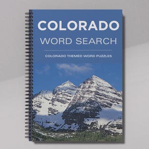 Peut inclure: Un livre à spirales intitulé "COLORADO WORD SEARCH" avec une couverture bleue représentant une chaîne de montagnes. Le texte "COLORADO THEMED WORD PUZZLES" est également visible. La reliure du livre est une spirale argentée.