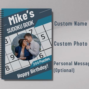 May include: A blue and gray personalized Sudoku book with a photo of a couple, the text "Mike's Sudoku Book", and the message "Happy Birthday! 200 Puzzles".