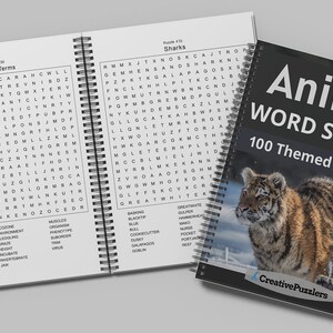 May include: A black and white book with the title "Animal Word Search 100 Themed Searches" and a picture of a tiger cub on the cover. The book is open to a page with a word search puzzle titled "Wildlife Terms".