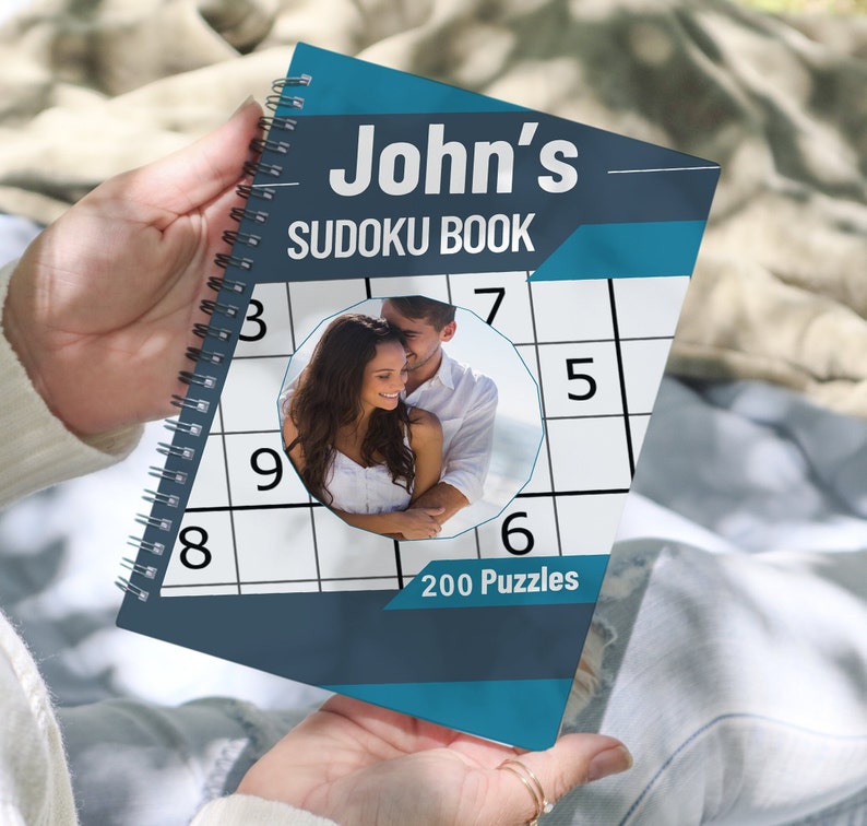 May include: A blue and gray spiral bound book with the title "John's Sudoku Book" and a photo of a couple on the cover. The book contains 200 puzzles.