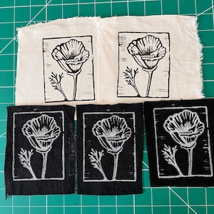 May include: Five fabric patches with a poppy flower design. Two patches are on a cream-colored fabric, and three are on black fabric. The poppy design is in black and white, with a detailed flower and stem.