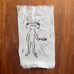 Pu&ograve; includere: Un'illustrazione in bianco e nero di una creatura che tiene una padella. La creatura ha una testa grande con due occhi grandi e una bocca larga. La creatura sta in piedi su due gambe e ha due braccia. La creatura tiene una padella in una mano. L'illustrazione &egrave; su uno sfondo di tessuto bianco.