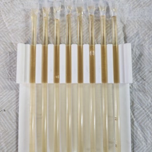 May include: A white plastic holder with ten clear plastic honey dippers. The dippers are filled with a light golden honey.