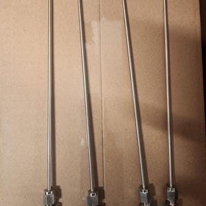 Puede incluir: Cuatro tubos de metal plateado con tapas de plástico azul en los extremos. Los tubos están dispuestos en una fila sobre una superficie marrón.