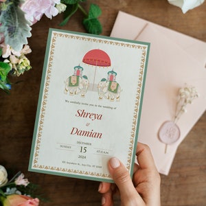 Puede incluir: Una invitación de boda con un borde verde y detalles dorados. La invitación presenta una ilustración de dos elefantes que llevan un dosel rojo y dorado. El texto dice "We cordially invite you to the wedding of Shreya & Damian, Sunday, December 15, 2024, at 11 a.m., 123 Anywhere St., Any City, ST 12345."