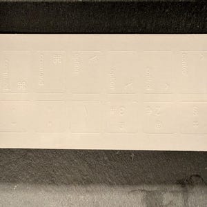 Könnte beinhalten: Weiße Tastaturaufkleber mit Beschriftungen für die Tasten Befehl, Option und Steuerung. Die Aufkleber enthalten auch Symbole für die Zifferntasten.