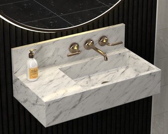 May include: A white marble bathroom sink with a gold faucet and soap dispenser. The sink is mounted on a black wall with vertical grooves. A round mirror with a black frame is mounted above the sink.