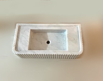 May include: White marble bathroom sink with a rectangular basin and a fluted base.
