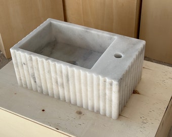 May include: A white marble sink with a fluted design. The sink has a rectangular shape and a small hole on the top.