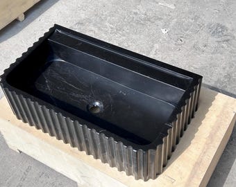 May include: A black marble sink with a fluted edge. The sink is rectangular and has a single drain hole.