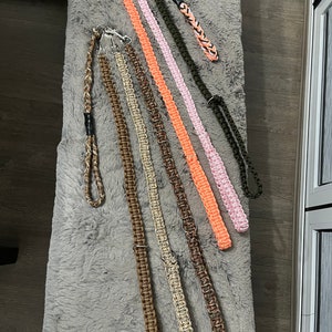 May include: A collection of eight colourful paracord leashes with metal clasps. The leashes are made of braided rope in various colours, including pink, orange, brown, and green.