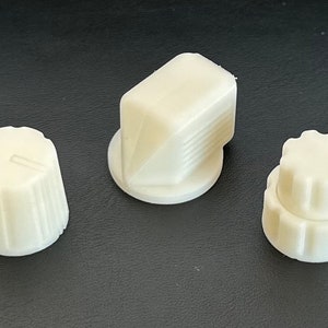 Könnte beinhalten: Drei weiße Kunststoffknöpfe für ein elektronisches Gerät. Ein Knopf ist rund mit einer flachen Oberseite, einer ist rund mit einer erhabenen Oberseite und einer ist quadratisch mit abgerundeten Kanten.