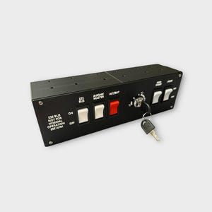 Könnte beinhalten: Ein schwarzes Panel mit mehreren Schaltern und einem Schlüssel. Die Schalter sind mit "ESS BUS", "AVIONIC MASTER", "ALT/BAT", "FUEL PUMP" und "BUSFLT" beschriftet. Das Panel hat auch ein Warnschild mit der Aufschrift "ESS BUS NOT FOR NORMAL OPERATION SEE AFM".