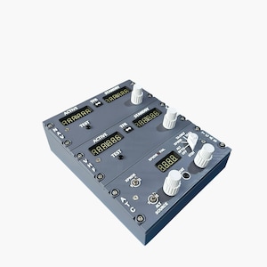 Puede incluir: Un panel de instrumentos de avión gris con múltiples pantallas digitales y perillas blancas. El panel tiene etiquetas de texto como "ACTIVE", "STANDBY" y "TEST". Las pantallas muestran lecturas numéricas. Diseñado para aviación.