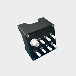 May include: A black electronic device with a white rotary knob and several white toggle switches. The device is rectangular with a slightly angled top and is secured with silver screws. The switches are arranged in two rows.