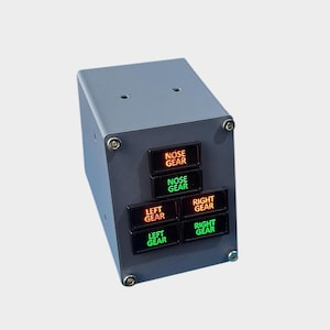 May include: A grey rectangular control panel with six illuminated buttons. The buttons are labelled "NOSE GEAR", "LEFT GEAR", and "RIGHT GEAR". The text is white, and the lights are red and green.
