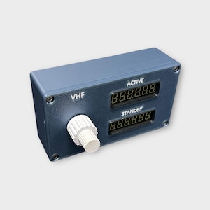 Può includere: Un pannello di controllo radio VHF blu scuro con display digitali per le frequenze ACTIVE e STANDBY. Il pannello ha una manopola bianca e il testo "VHF". I display digitali mostrano i numeri "8.8.8.8.8.8."