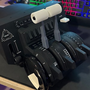 May include: A black flight simulator control panel with multiple knobs, switches, and levers. The panel features a gear lever, flap lever, and a trim wheel. The panel is labeled "FLAPS" and "GEAR".