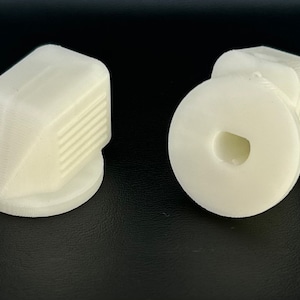 May include: Two white plastic knobs, one with a smooth surface and the other with a textured surface. The knobs are designed for use with furniture or appliances.