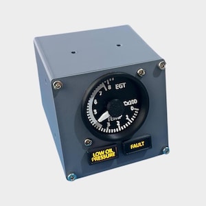 Könnte beinhalten: Ein graues rechteckiges Instrumentenfeld mit einer kreisförmigen Anzeige, die "EGT" und Zahlen anzeigt. Unter der Anzeige befinden sich zwei rechteckige Knöpfe mit der Aufschrift "LOW OIL PRESSURE" und "FAULT". Der Zeiger der Anzeige zeigt auf die Zahl 6.