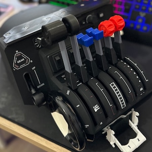 Puede incluir: Un panel de control de simulador de vuelo negro con cinco palancas, cada una con una perilla roja o azul. El panel tiene una palanca de cambios con las etiquetas 'N', 'GEAR', 'R', 'UP' y 'DOWN'. El panel también tiene un dial con las etiquetas 'FLIGHT DETENT' y '150M'.