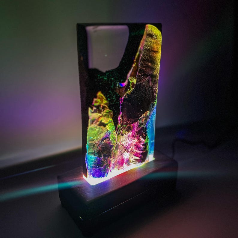 May include: A black wooden base with a clear resin lamp. The resin has a swirling pattern of iridescent colors, including green, blue, pink, and purple.