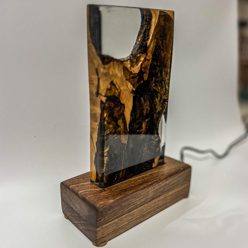 May include: A wooden base with a clear resin panel featuring a swirling pattern of black, brown, and white. The resin panel is illuminated from behind, creating a warm glow.