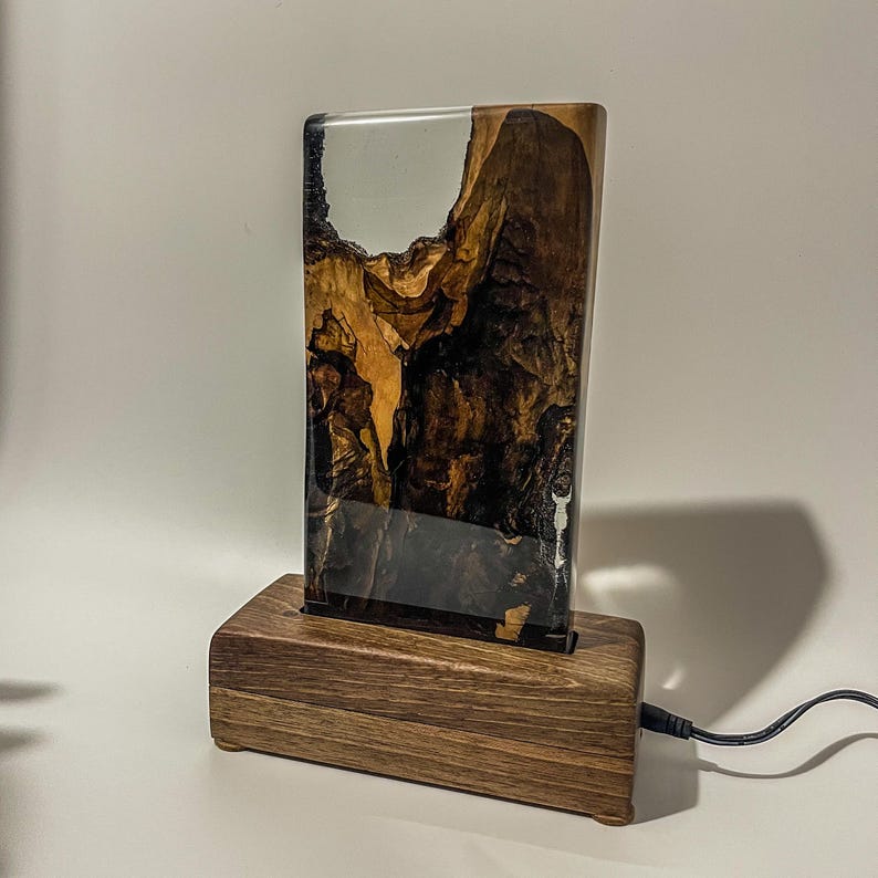 May include: A wooden base with a clear resin block featuring a natural wood grain pattern. The resin block is illuminated from behind, creating a warm glow.