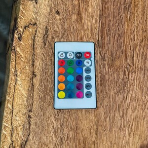 May include: A white remote control with a variety of colored buttons. The buttons are arranged in a grid and labeled with letters and words, including "R", "G", "B", "W", "Flash", "Strobe", "Fade", and "Smooth".