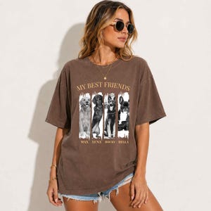 Puede incluir: Una camiseta marrón de manga corta con el texto MY BEST FRIENDS en dorado. Debajo del texto hay cuatro paneles verticales que muestran retratos de perros en blanco y negro con los nombres MAX, LUNA, ROCKY y BELLA impresos en dorado bajo cada perro.