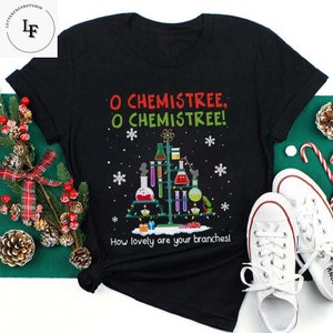 Könnte beinhalten: Schwarzes T-Shirt mit einem Weihnachtsbaum-Design aus Laborgeräten und dem Text "O Chemistree, O Chemistree! How lovely are your branches!" Weiße Turnschuhe sind rechts.