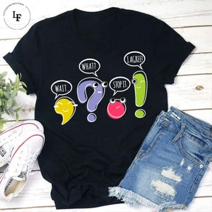 May include: Black t-shirt featuring a graphic of punctuation marks with faces and speech bubbles. The speech bubbles say "Wait", "What?", "Stop it", and "I agree!"