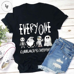 May include: Black t-shirt with a white graphic of four Halloween characters and the text "Everyone Communicates Different".