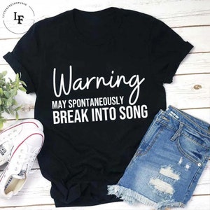 Puede incluir: Camiseta negra con texto blanco que dice "Warning May Spontaneously Break Into Song".