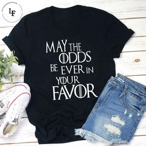 May include: Black t-shirt with white text that reads "May the odds be ever in your favor".