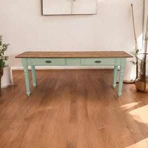 Pode incluir: Uma mesa de fazenda azul claro com duas gavetas e tampo de madeira. A mesa está sobre um piso de madeira dura.