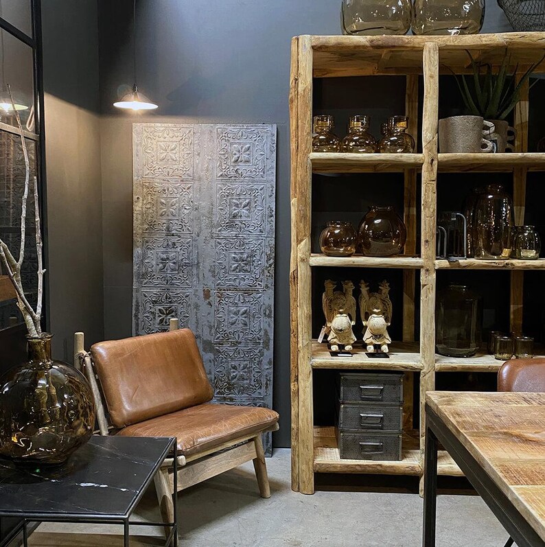 May include: A rustic wooden shelving unit with multiple shelves, displaying various decorative items, including glass bottles, vases, and figurines. A brown leather armchair sits in front of the shelving unit, with a black metal side table next to it.