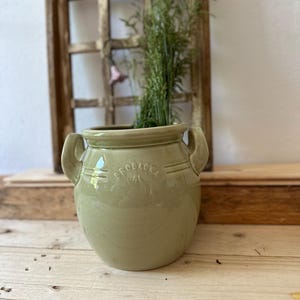 Könnte beinhalten: Ein grüner Keramiktopf mit zwei Henkeln und dem Text "GRÖBACKA 1.4L" an der Seite. Der Topf steht auf einer Holzoberfläche.