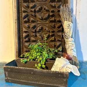 Puede incluir: Dos moldes para pasteles de metal vintage con una planta verde en uno de los moldes. Los moldes están sobre una superficie azul. Un manojo de lavanda seca está en el fondo.