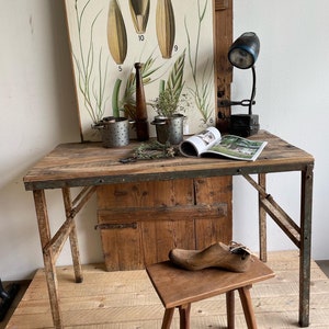 May include: A rustic wooden table with metal legs, a wooden stool, and a vintage lamp. The table has a distressed finish and is perfect for a workshop or studio. There are also a few decorative items on the table, including a book, a pair of scissors, and a few small metal containers.