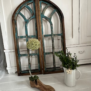 Può includere: Due cornici ad arco in legno anticato con vernice turchese e marrone. Un'ultima scarpa in legno contiene vegetazione e una brocca bianca con vegetazione e un ornamento a stella in legno è nelle vicinanze. Arredamento per la casa.