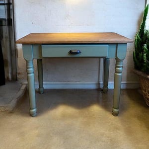 Peut inclure: Un petit bureau en bois avec un seul tiroir et des pieds tournés. Le bureau est peint en vert sauge clair avec un plateau en bois naturel. Le tiroir a une poignée en métal noir.