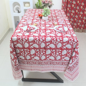 Puede incluir: Mantel de mesa de algodón rojo y blanco con un patrón floral. El mantel tiene un borde blanco con un diseño geométrico repetitivo.