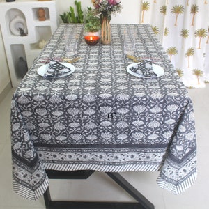 Puede incluir: Un mantel de mesa negro y blanco con estampado floral y borde blanco. El mantel está puesto sobre una mesa con dos cubiertos, incluyendo platos, servilletas y vasos.