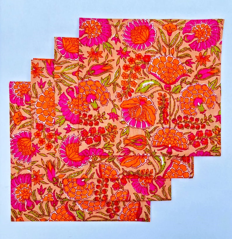 May include: Set of four pink and orange floral cotton napkins. The napkins feature a repeating pattern of pink and orange flowers on a light pink background.