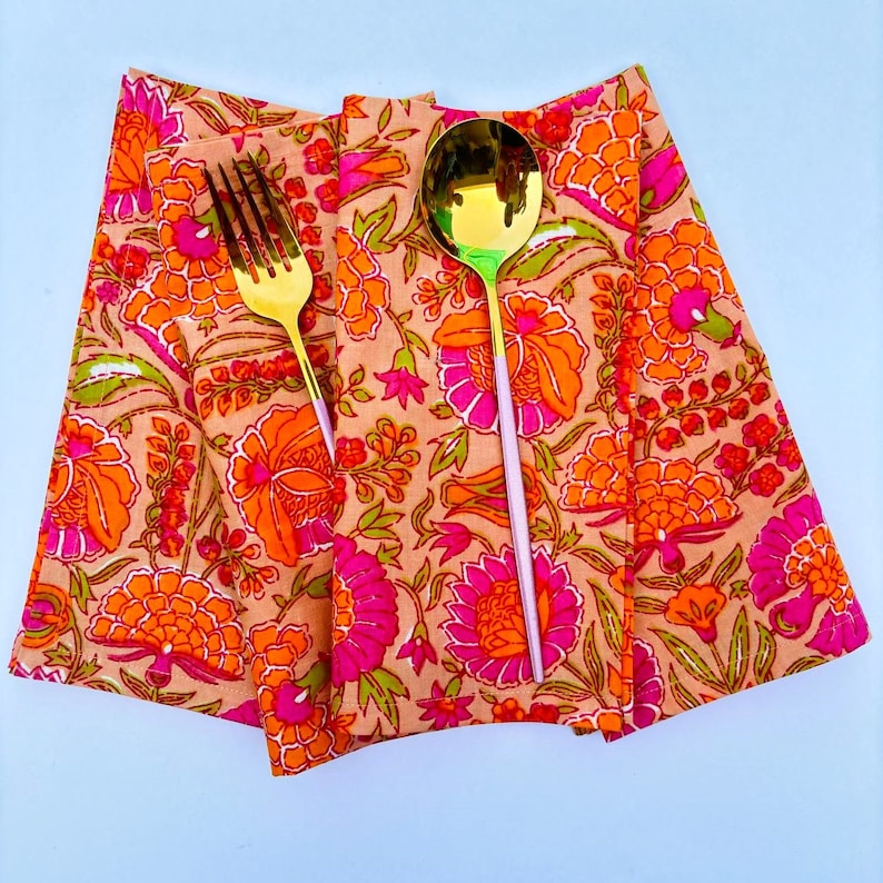 May include: Three orange and pink floral print napkins with a gold fork and spoon on top.