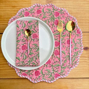 Könnte beinhalten: Rosa-farbener Platzdeckchen aus Baumwolle mit Blumenmuster, gewelltem Rand und weißem Besatz. Auf dem Platzdeckchen liegt ein weißer Teller mit einer rosa-farbener Serviette mit Blumenmuster und goldenem Besteck.