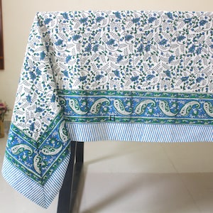 Puede incluir: Mantel blanco con un borde de paisley azul y verde. El mantel tiene un patrón floral con flores azules y hojas verdes.